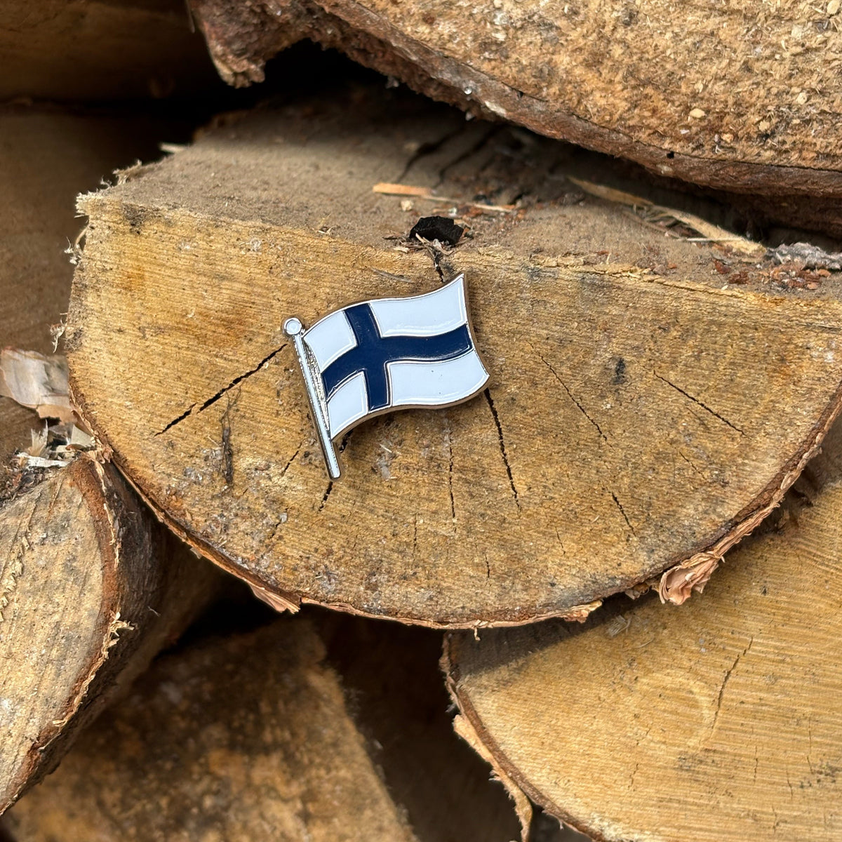 Finnish Flag enamel pin on a stack of firewood