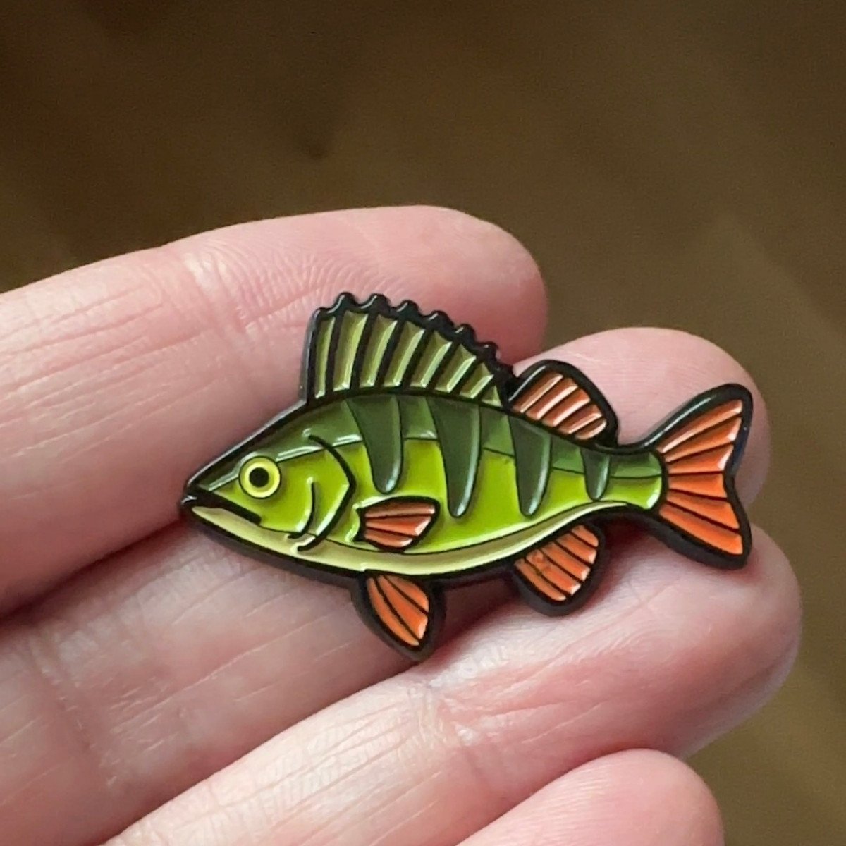 Ahven-pinssi kädessä, vihreä-oranssi yksityiskohta.